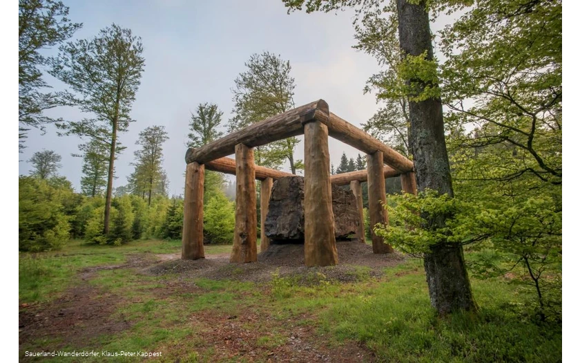 Die Holzstämme umringen den Stein der Stein-Zeit-Mensch Skulptur