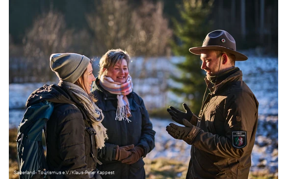 Ein Ranger erklärt zwei lachenden Wanderinnen die Natur im Schwarzbachtal