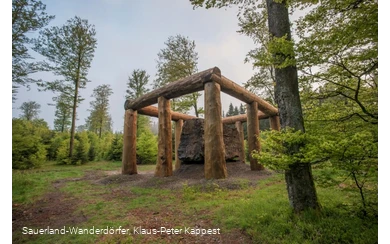 Die Holzstämme umringen den Stein der Stein-Zeit-Mensch Skulptur