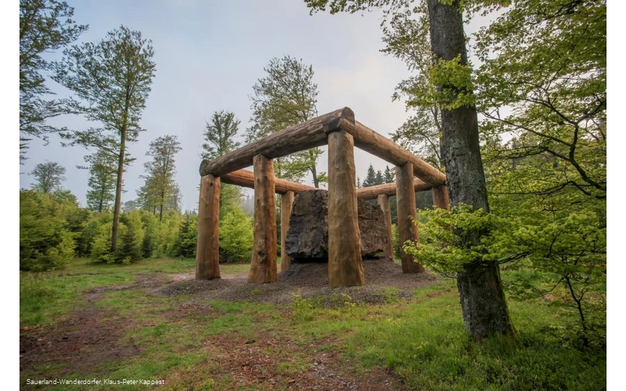 Die Holzstämme umringen den Stein der Stein-Zeit-Mensch Skulptur