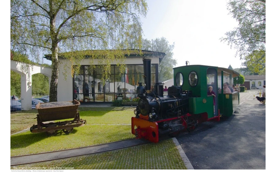 Menschen sitzen in einer fahrenden grünen Lok auf dem Museumsgelände