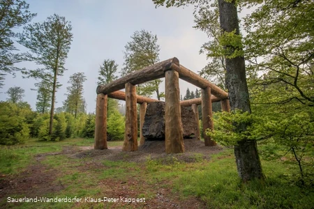 Die Holzstämme umringen den Stein der Stein-Zeit-Mensch Skulptur