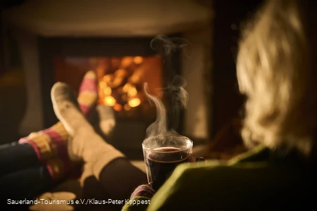 Eine Frau genießt mit einer heißen tasse Tee den Winterbane dvor dem Kamin