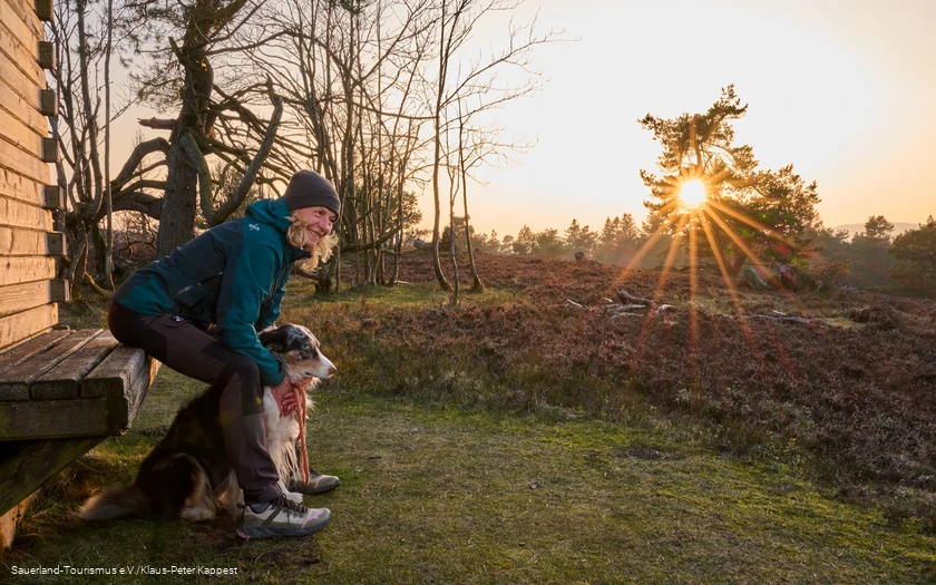 Frau mit Hund an Hütte Eine Frau sitzt mit einem Hund an einer Hütte im Sonneuntergang auf der Kahlen Pön in Willingen