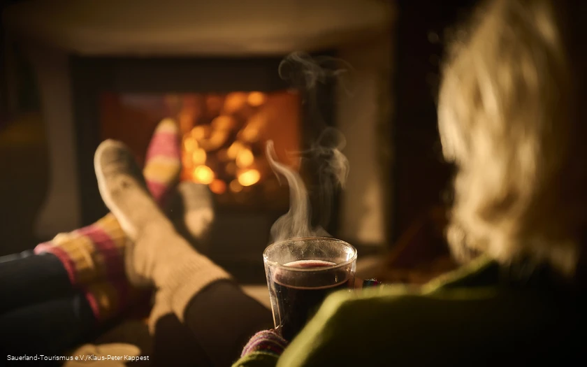 Eine Frau genießt mit einer heißen tasse Tee den Winterbane dvor dem Kamin