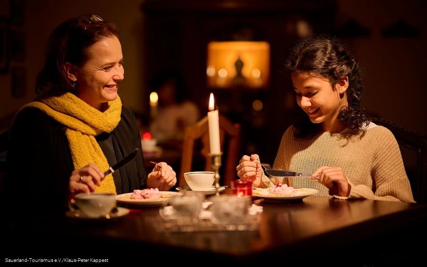 Eine Mutter mit ihrer Tochter sitzen bei gemütlichem Kerzenlicht an der Kaffeetafel mit Waffeln