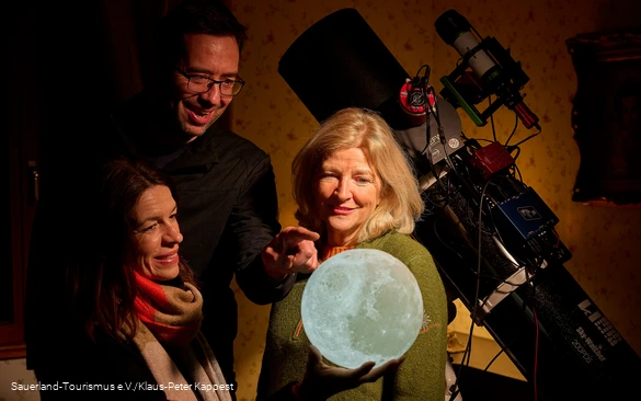 Drei Menschen schauen auf ein leuchtenes Mondmodell als Vorbereitung zum Sternegecken