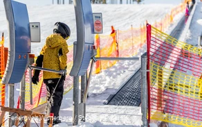 Kind geht mit Schlitten durch ein Drehkreuz zum Förderband.