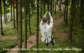 Eine Person fliegt an einem Gurt und Seil gesichert von einem Baum zum nächsten.