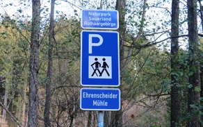 Blaues Schild für einen Wanderparkplatz mit einem weißen P und zwei wandernden Strichmännchen, sowie der Aufschrift Ehrenscheider Mühle.