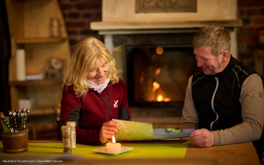Eine Frau und ein Mann stidieren die Speisekarte in der Graf Stolberg Hütte, vor einem Kamin
