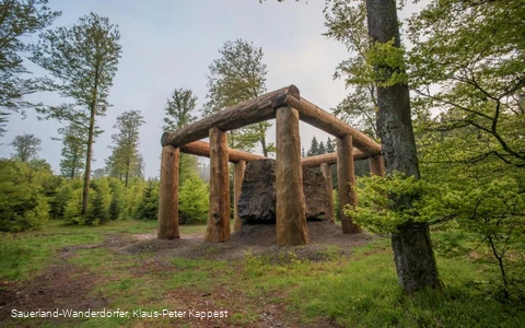 Die Holzstämme umringen den Stein der Stein-Zeit-Mensch Skulptur