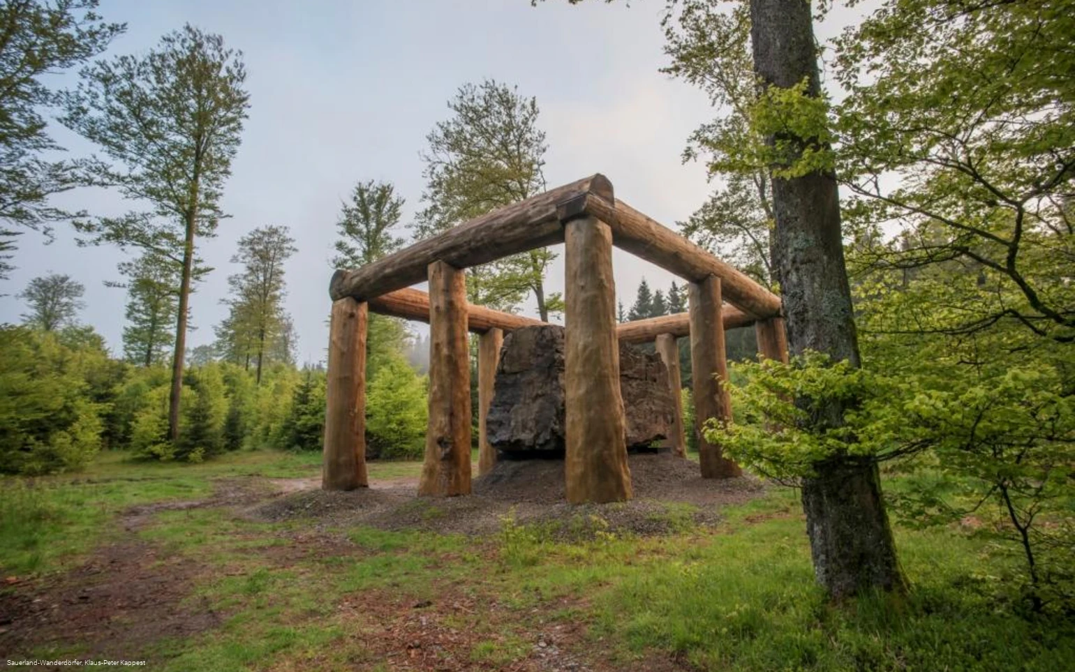 Die Holzstämme umringen den Stein der Stein-Zeit-Mensch Skulptur