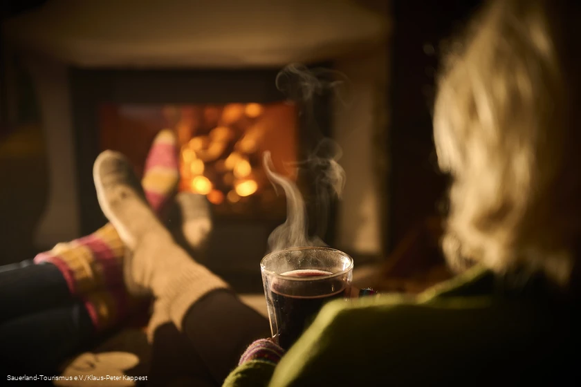Eine Frau genie&szlig;t mit einer hei&szlig;en tasse Tee den Winterbane dvor dem Kamin