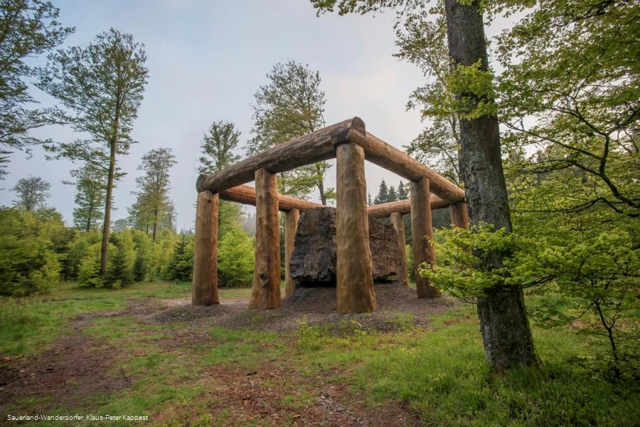 Die Holzstämme umringen den Stein der Stein-Zeit-Mensch Skulptur