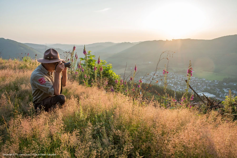 Ein Ranger sitzt am Rothaarkamm im Gras und fotografiert