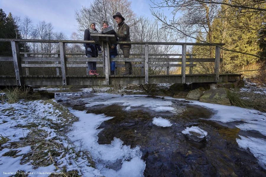 Zwei Wanderinnen mit einem Ranger auf einer Br&uuml;cke im Schwazbachtal an einem kalten Wintermorgen