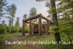 Die Holzstämme umringen den Stein der Stein-Zeit-Mensch Skulptur