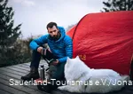 Ein Wanderer sitzt auf einem Trekkingplatz in Hallenberg mit seinem Hund vor einem Zelt