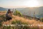 Ein Ranger sitzt am Rothaarkamm im Gras und fotografiert