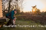 Eine Frau sitzt mit einem Hund an einer Hütte im Sonneuntergang auf der Kahlen Pön in Willingen