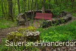 Eine rote Bank steht in einem Kreis aus Holzscheiten, die sogenannte Dichterlichtung