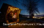 Drei Menschen sitzen im Unterstand im Dunkeln, in der Ferne leuchten die Lichter eines Dorfes
