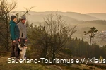 Ein Wanderpaar mit Hund im Abendlicht im Hintergrund der Ettelsberg