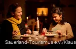 Eine Mutter mit ihrer Tochter sitzen bei gemütlichem Kerzenlicht an der Kaffeetafel mit Waffeln